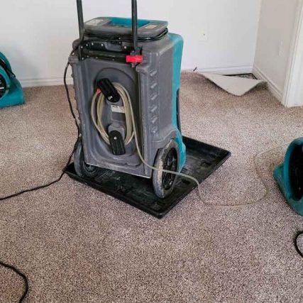 Industrial dehumidifiers are set up in a carpeted room to address water damage