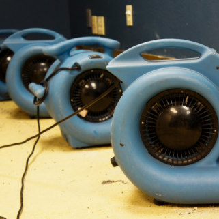 Three blue industrial fans placed on a floor in a room with dark blue walls