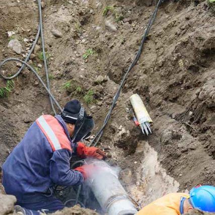 Workers repair a large pipe in a muddy trench